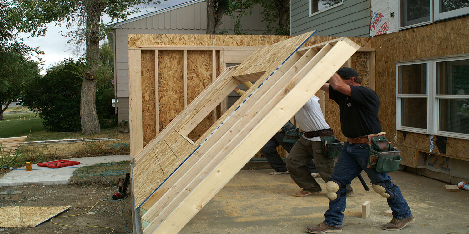 House flipping renovation with builders raising new wall.